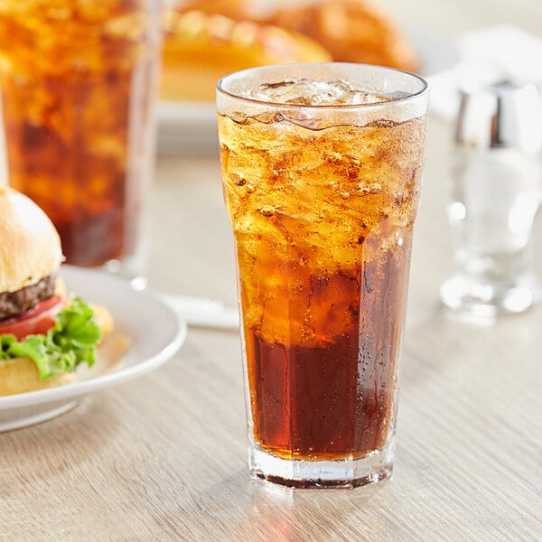A Pasabahce Casablanca cooler glass of brown liquid with ice on a table with a burger.