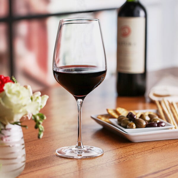 A Nude Refine red wine glass filled with red wine sits on a table.