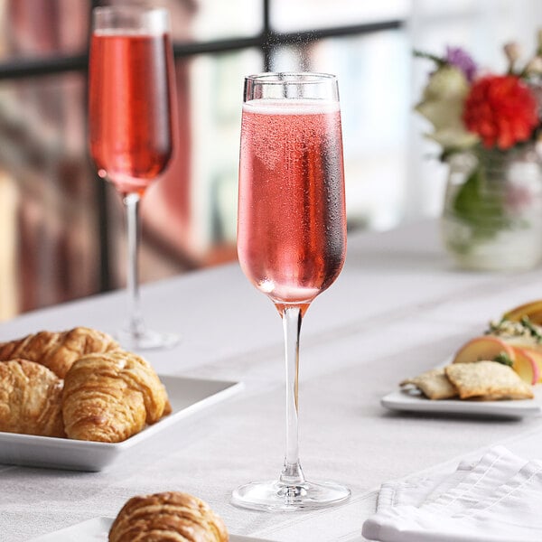 A table with a Nude Refine flute of pink liquid and pastries.