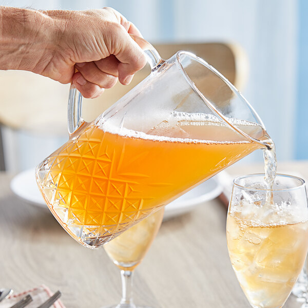 A hand pouring a glass of liquid from a Pasabahce Timeless Vintage glass pitcher.