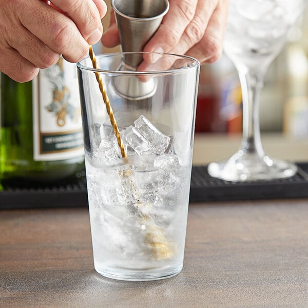 A person mixing a drink in a Pasabahce tempered mixing glass on a counter.