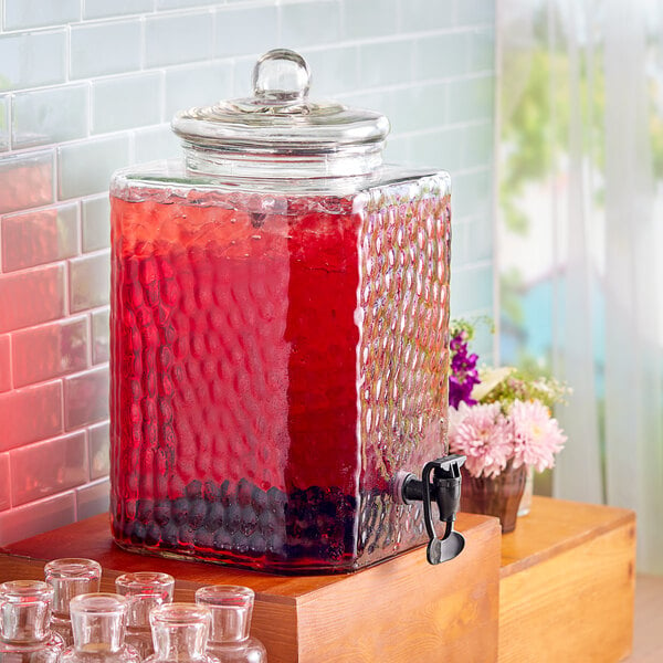 An Acopa glass beverage dispenser filled with red liquid on a counter.