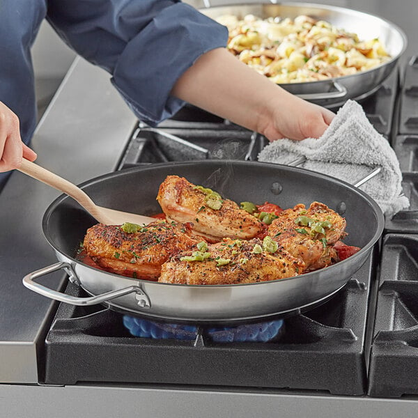 A woman cooking food in a Vigor stainless steel non-stick fry pan with dual handles.