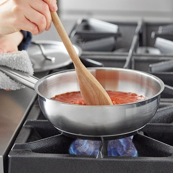 A person stirring food in a Vigor stainless steel saucier pan on a stove with a wooden spoon.