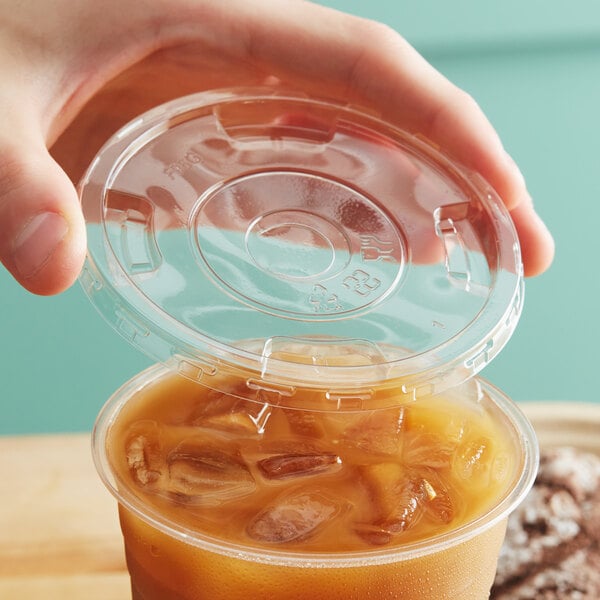 A hand placing an EcoChoice PLA compostable plastic lid on a plastic cup with a brown liquid and ice.