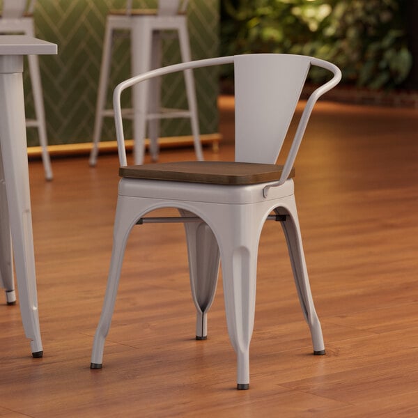 A white metal Lancaster Table & Seating arm chair with a walnut wood seat.