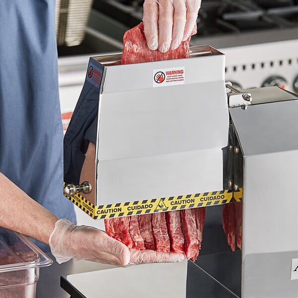 A person holding a meat machine attachment and using it to tenderize meat on a counter.