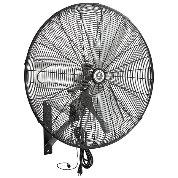 A close-up of a black TPI wall-mounted industrial fan with a wire cage and cord attached.