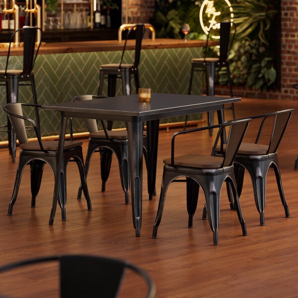 A Lancaster Table & Seating Alloy Series distressed onyx black table with walnut seats and 4 chairs with legs.