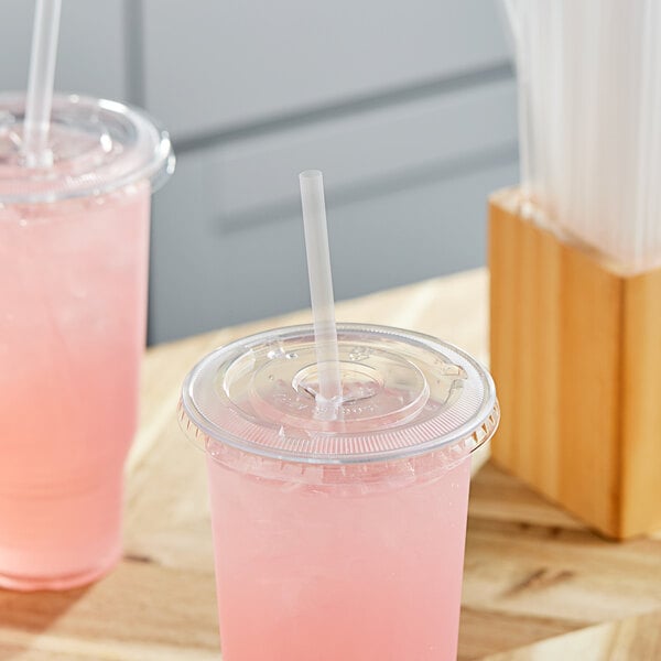 A couple of plastic cups with pink liquid and Choice giant translucent wrapped straws.