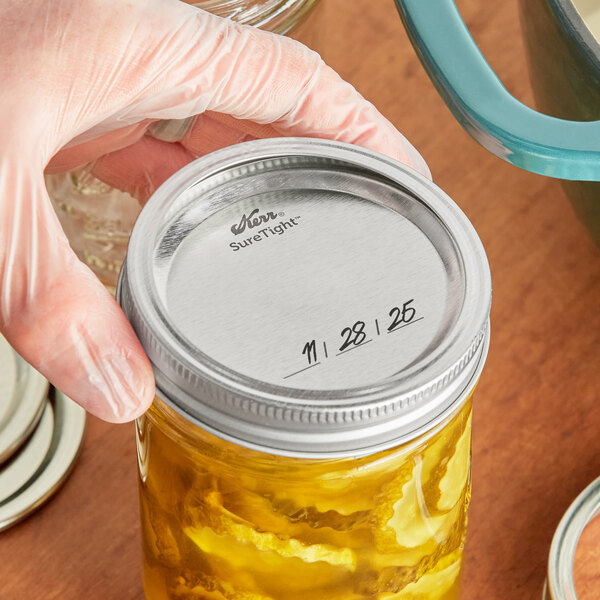 A hand holding a Kerr canning jar of pickles with a silver lid.