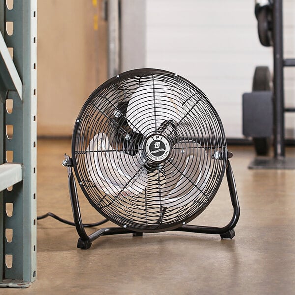 A black TPI industrial floor fan on a warehouse floor.