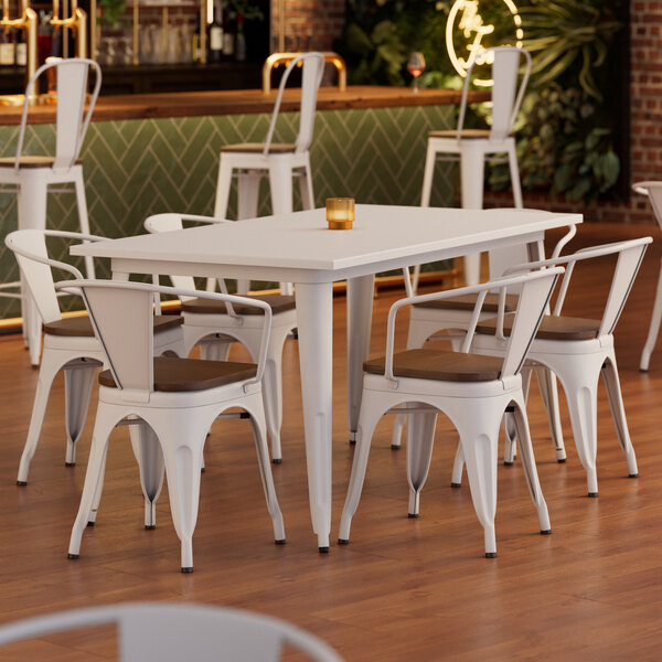 A white table with a brown edge and 6 white chairs with walnut wood seats.