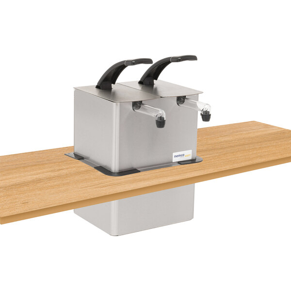 A silver rectangular Nemco stainless steel pump dispenser with black handles on a wooden surface.