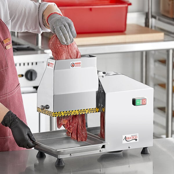 A woman using an Avantco meat tenderizer to cut meat on a counter.