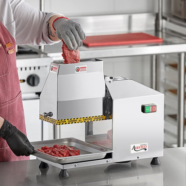 A person in a red apron and black glove using the Avantco meat tenderizer to cut meat.