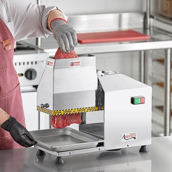 A person using an Avantco meat tenderizer on a metal counter.