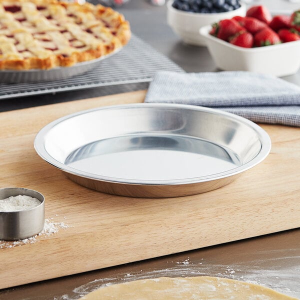 A Baker's Mark pie pan on a cutting board with a pie and a bowl of strawberries.