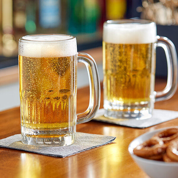 Two Libbey beer mugs filled with beer on a table.