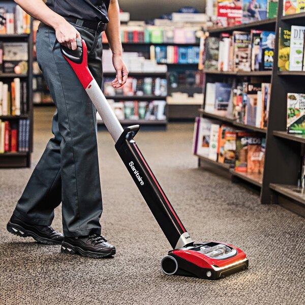A woman using a Sanitaire TRACER cordless upright vacuum cleaner in a store.