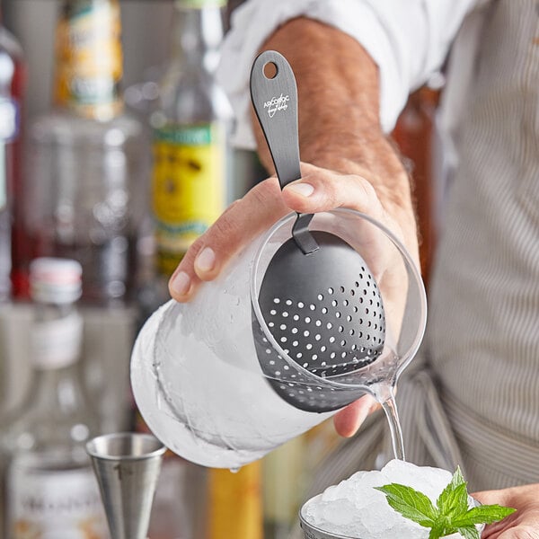 A man using an Arcoroc stainless steel julep strainer to pour a drink into a glass.