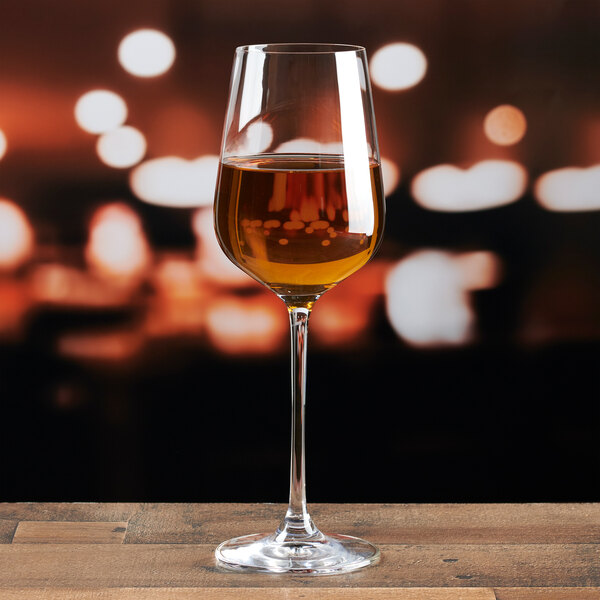 A clear Lucaris Hip Chardonnay wine glass partially filled with white wine, placed on a wooden surface.