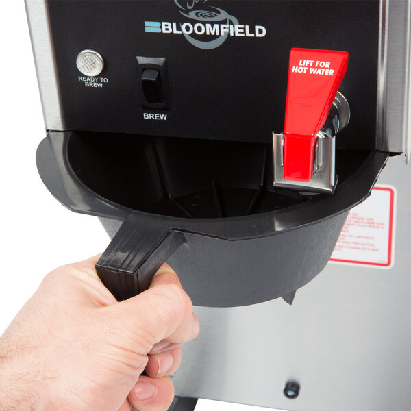 A person holding a Bloomfield airpot coffee brewer over a counter.
