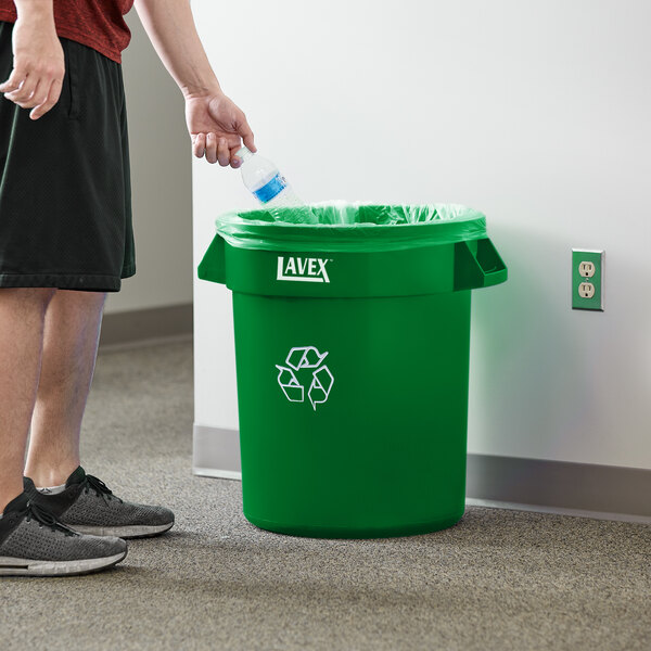 A man putting a plastic bottle into a green Lavex commercial recycling can.