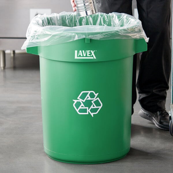 A man in a black suit recycling a water bottle in a green Lavex recycling can.