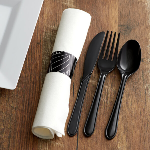 A white napkin with black silverware pre-rolled in paper.