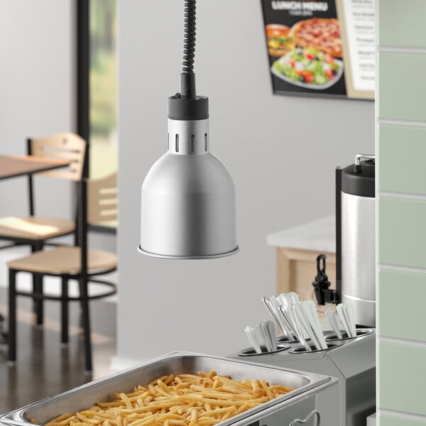 A ServIt chrome ceiling mount heat lamp over a container of french fries.