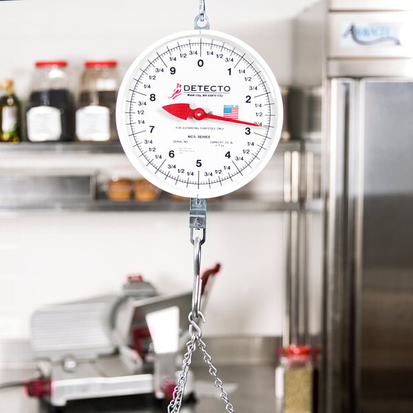 A Cardinal Detecto hanging hook scale on a white counter.