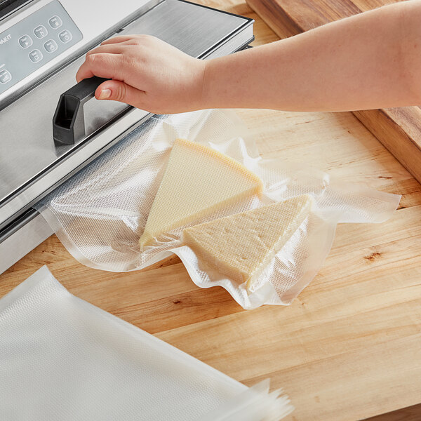 A hand using a Choice gallon size mesh vacuum packaging bag to vacuum seal a triangular piece of cheese.