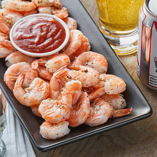 Large sized peel and eat shrimp on a serving platter with a dish of cocktail sauce in the center