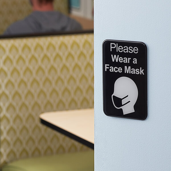 A Tablecraft plastic wall sign that says "Please Wear a Face Mask" in black and white text.