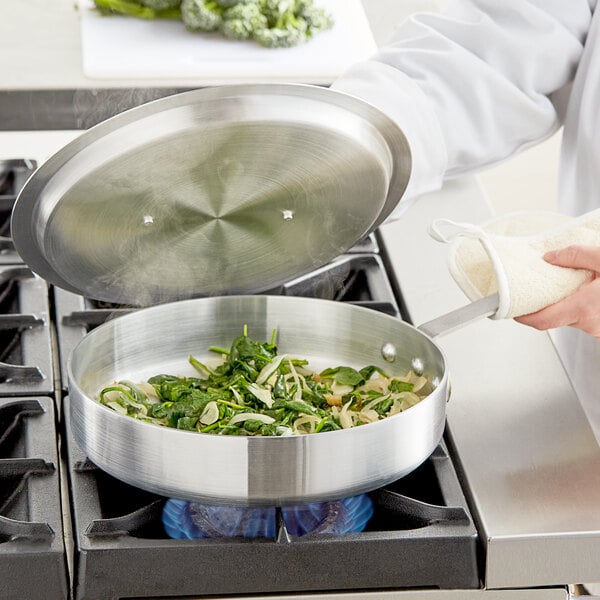 A person cooking vegetables in a Choice aluminum saute pan on a stove.