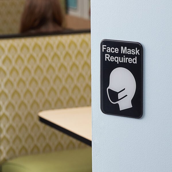 A Tablecraft plastic sign on a wall that says "Face Mask Required" in black and white.