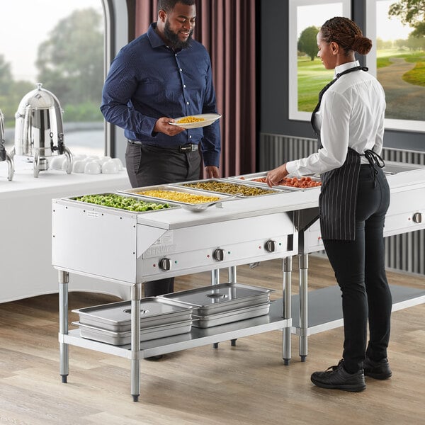 A man and woman serving food from a ServIt electric steam table at a hotel buffet.