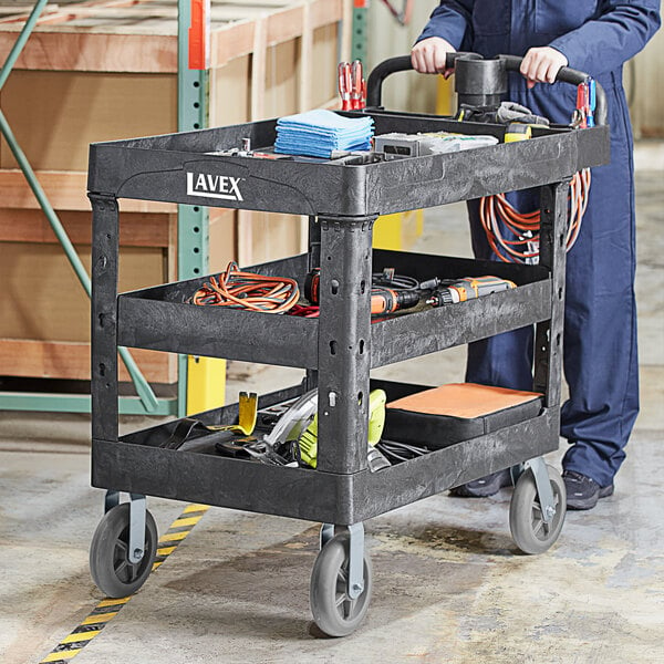 A man pushing a Lavex black utility cart with tools on it.