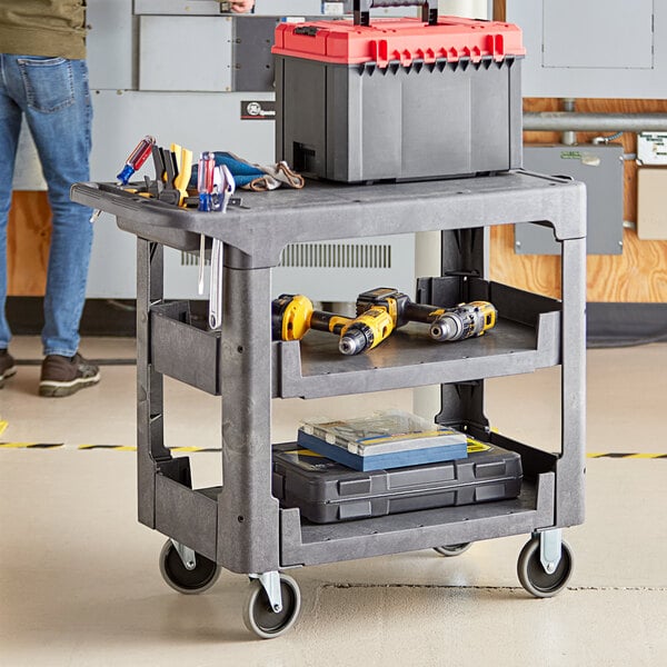 A man standing next to a Lavex medium gray utility cart with tools in it.
