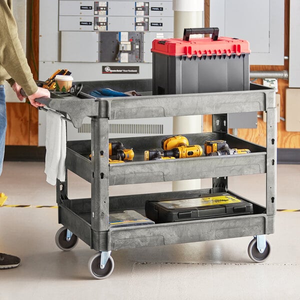 A man standing next to a Lavex large gray utility cart with tool compartments holding a tool.