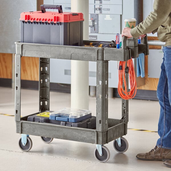 A man using a Lavex medium gray utility cart with tools on it.