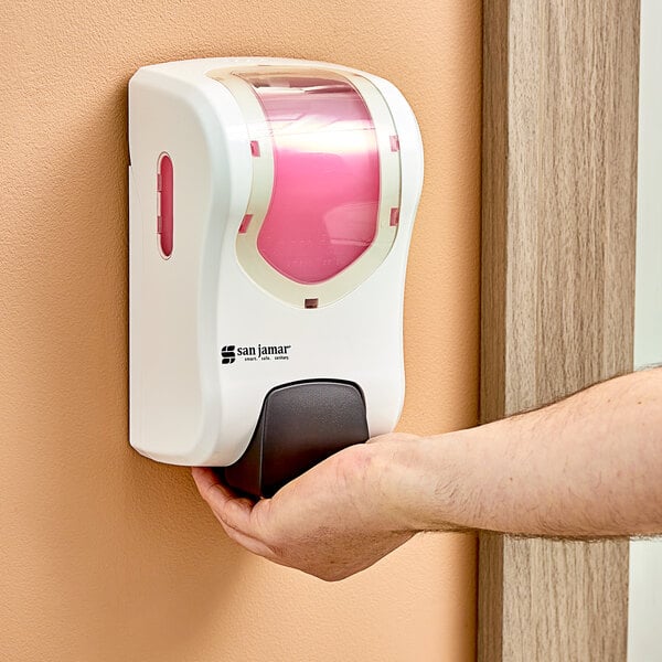 A person using a white and pink San Jamar Summit Rely manual foam hand soap and sanitizer dispenser.