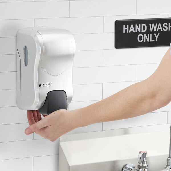 A white San Jamar manual hand soap, sanitizer, and lotion dispenser on a wall.