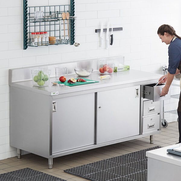 A man using a Regency stainless steel enclosed base table in a kitchen.