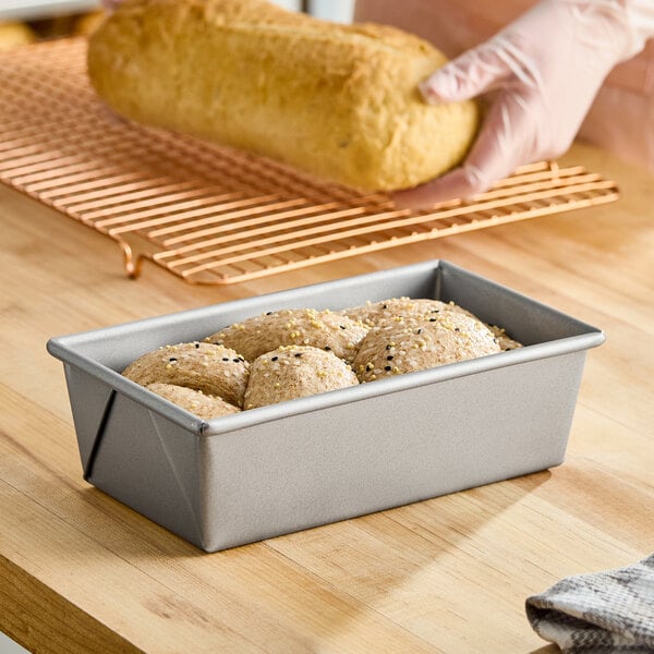 A rectangular glazed aluminized steel bread loaf pan filled with dough, measuring 8 1/2 inches by 4 1/2 inches by 2 3/4 inches.