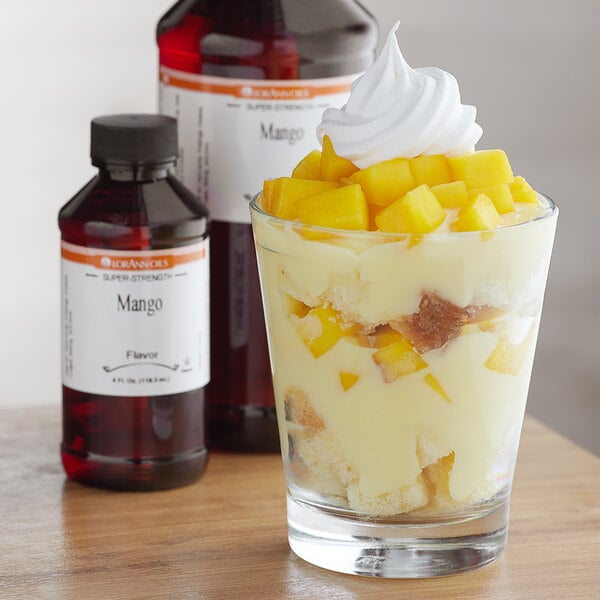 A glass of dessert with white frosting and fruit with LorAnn Oils Mango Flavor on a table.