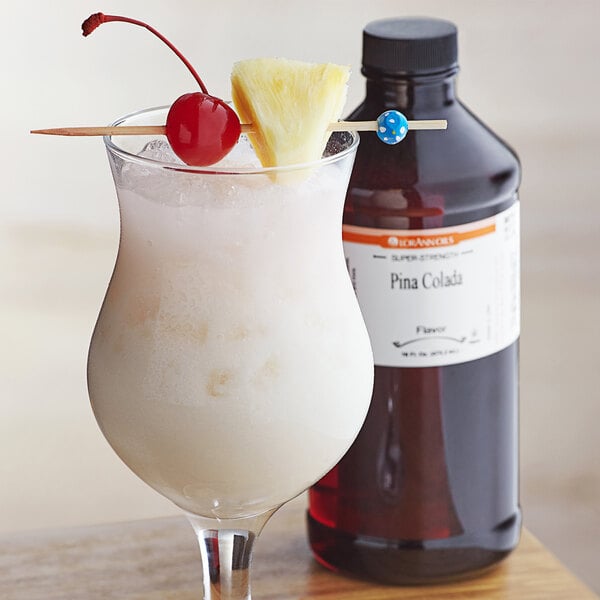 A glass of white liquid with a cherry and pineapple on top next to a bottle of LorAnn Oils Pina Colada Super Strength Flavor.