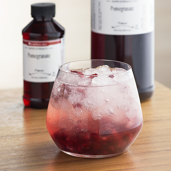 A glass of red liquid with ice and a bottle of LorAnn Oils Pomegranate Super Strength Flavor.