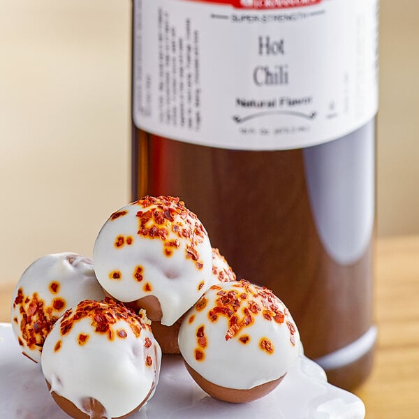 A group of round white and red balls with white frosting on them with a bottle of LorAnn Oils hot chili flavor on the side.